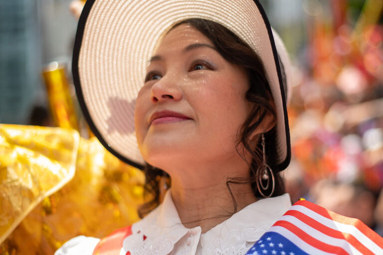 A brightly lit asian woman is holding an american flag and looking up